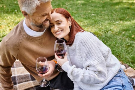 Ein Mann und eine Frau genießen Wein auf einer Decke in einem Park.