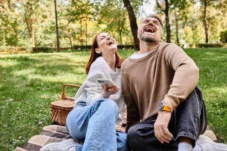 A man and woman, a loving couple, sit on a blanket laughing joyfully.