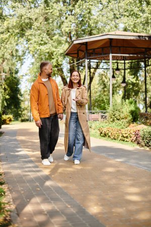 Photo for A man and a woman in casual attire walk hand in hand down a peaceful path. - Royalty Free Image