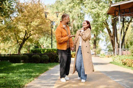 A man and a woman in casual attire walking down a sidewalk in a park.