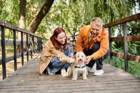 Man and woman lovingly pet a dog on a bridge in the park.