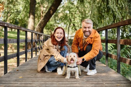 A couple kneels with their dog in a peaceful park setting.