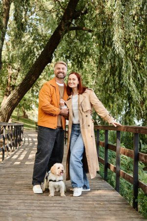 Erwachsenes Paar in Freizeitkleidung steht mit seinem geliebten Hund auf einer Brücke.