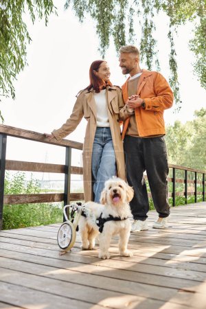 Un couple et leur chien profitent d'un moment paisible sur un pont dans le parc.