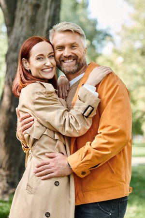 Foto de Un hombre y una mujer se abrazan amorosamente en un parque mientras caminan tranquilamente. - Imagen libre de derechos