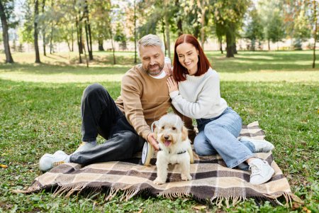 A couple with their dog relaxes on a blanket in the park.