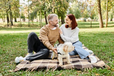 Photo for A man and woman sit on a blanket with their dog. - Royalty Free Image