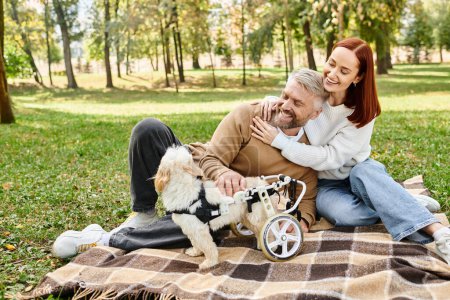 A man and woman relax on a blanket with their dog in a serene park.