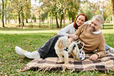 Photo for A man and woman relax on a blanket with their dog in a peaceful outdoor setting. - Royalty Free Image