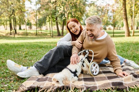 Ein Paar in Freizeitkleidung sitzt mit seinem Hund auf einer Decke in einer friedlichen Parklandschaft.