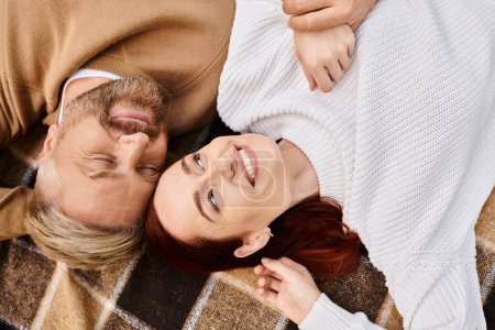Téléchargez les photos : Un homme et une femme en tenue décontractée sont tranquillement couchés ensemble sur une couverture à carreaux. - en image libre de droit