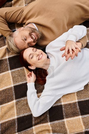 A man and a woman lay peacefully on a blanket in a park.