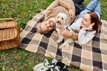Foto de Una pareja se relaja en una manta con su perro en un hermoso entorno de parque. - Imagen libre de derechos