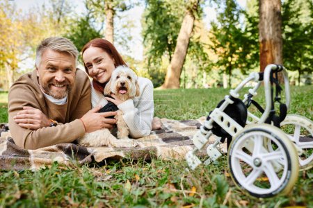 Photo for A couple relaxes on a blanket with their dog in a park. - Royalty Free Image