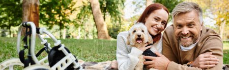 Photo for A man and woman in casual attire relax on grass with a dog by their side. - Royalty Free Image