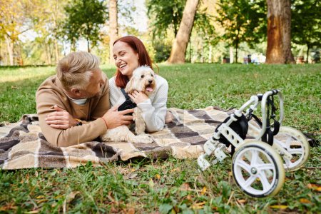 Foto de Un hombre y una mujer se relajan en una manta con su perro en un entorno al aire libre sereno. - Imagen libre de derechos