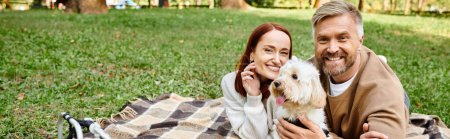 Photo for A man and woman enjoy a peaceful moment on a blanket with their dog in a park. - Royalty Free Image