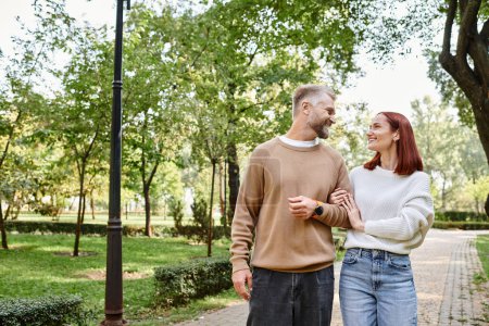 A man and a woman, a loving couple, walk together in casual attire in a peaceful park setting.