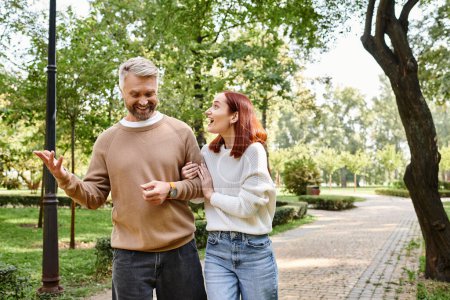 Ein liebevolles erwachsenes Paar in Freizeitkleidung geht in einem Park einen Bürgersteig entlang.