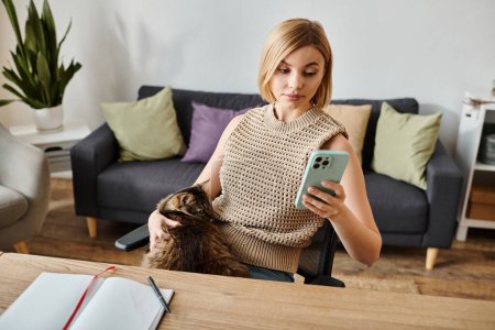Une femme aux cheveux courts s'assoit à une table avec son chat, faisant défiler son téléphone portable, profitant d'un moment de détente à la maison.