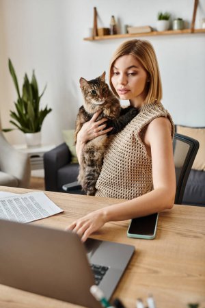 Téléchargez les photos : Une femme élégante aux cheveux courts assise à une table travaillant sur un ordinateur portable avec son chat à ses côtés. - en image libre de droit