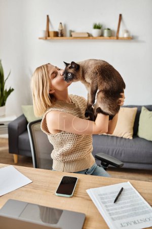 Téléchargez les photos : Une femme élégante avec des cheveux courts collant avec son chat bien-aimé en le tenant dans ses mains à la maison. - en image libre de droit
