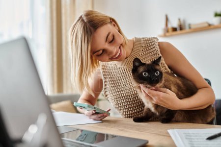 Eine Frau mit kurzen Haaren sitzt an einem Schreibtisch und hält liebevoll eine Katze im Arm..