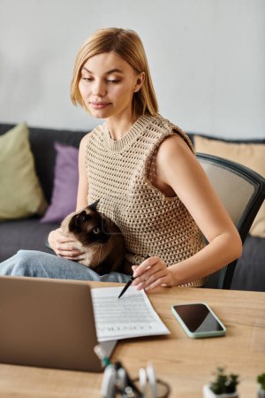 Una mujer con el pelo corto absorto en su trabajo portátil, acompañada por su gato contenido en una mesa acogedora.