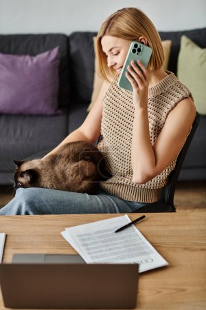 Una mujer elegante con el pelo corto se relaja en un sofá, centrado en su teléfono celular, mientras que su gato contento descansa en su regazo.