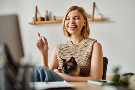 A woman with short hair sits at a desk, peacefully interacting with her cat at home.