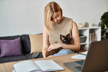 Eine zufriedene Frau mit kurzen Haaren sitzt mit ihrer Katze auf dem Schoß an einem Tisch und genießt einen friedlichen Moment zu Hause.