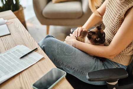 Eine stylische Frau mit kurzen Haaren sitzt auf einem Stuhl und hält ihre Katze liebevoll zu Hause.