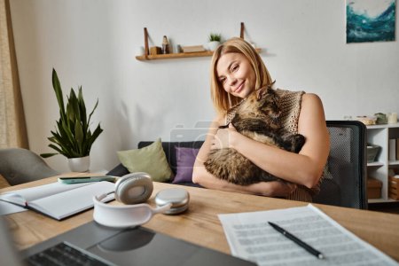 Eine Frau mit kurzen Haaren sitzt an einem Tisch und hält ihre Katze sanft in einem friedlichen und liebevollen Moment zu Hause.