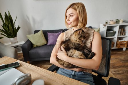 A stylish woman with short hair relaxes in a chair, gently cradling her content feline companion.
