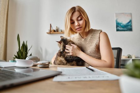 Una mujer con el pelo corto se sienta tranquilamente en un escritorio, sosteniendo suavemente a su gato en sus manos.