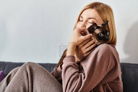 Une femme aux cheveux courts se détend sur un canapé, tenant son chat avec amour dans ses bras.