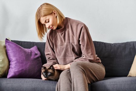 Eine Frau mit kurzen Haaren entspannt sich auf einer Couch, wiegt ihre Katze auf dem Arm und verbringt einen friedlichen Moment miteinander.
