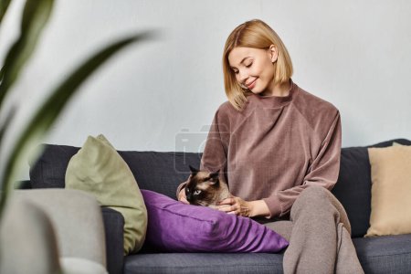 Una mujer serena con el pelo corto se relaja en un sofá, sujetando suavemente a su amado gato cerca de su pecho.