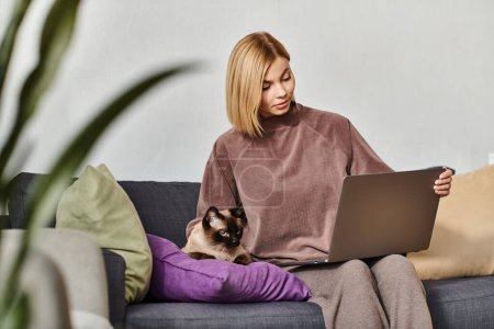 Kurzhaarige Frau genießt die Zeit zu Hause mit Laptop und Katze auf der Couch.