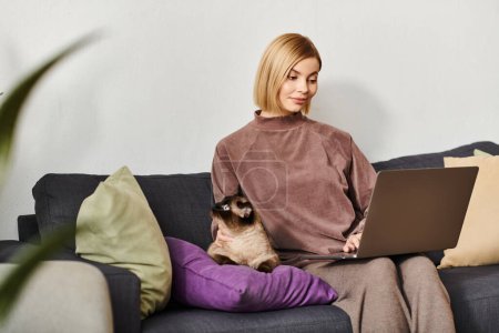 Una mujer atractiva con el pelo corto descansa en un sofá, sonriendo, como un gato contenido descansa en su regazo.