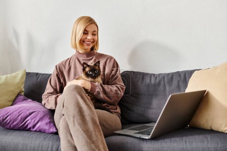 Photo for A woman with short hair relaxing on a couch with a cat perched on her lap. - Royalty Free Image