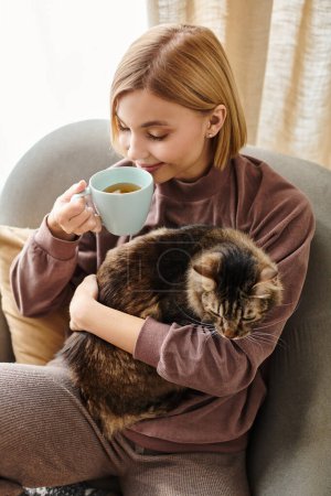 Eine Frau mit kurzen Haaren sitzt friedlich auf einem Stuhl und hält eine Katze auf ihrem Schoß, während sie eine Tasse Kaffee genießt.