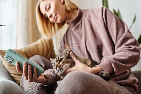A stylish woman with short hair serenely sits on a couch holding her beloved cat.