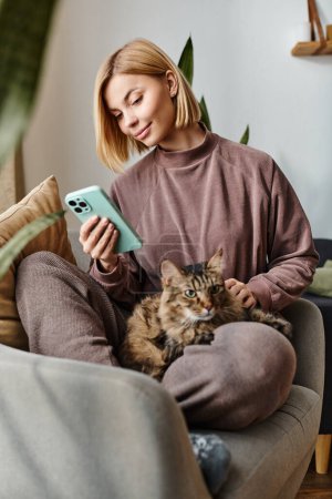 Téléchargez les photos : Une jolie femme aux cheveux courts s'assoit sur un canapé, tenant son chat dans un moment paisible et intime à la maison. - en image libre de droit