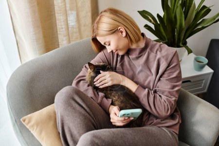 Una mujer con el pelo corto se relaja en una silla, abrazando amorosamente a su gato en un ambiente acogedor en casa.
