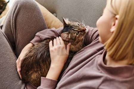 A woman with short hair reclining on a couch, tenderly petting her cat with a serene expression.