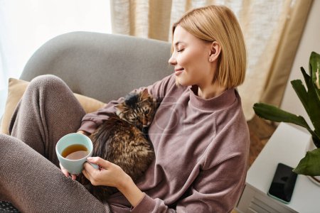 Eine stilvolle Frau lümmelt auf einer Couch, genießt Tee und kuschelt eine zufriedene Katze in einer ruhigen häuslichen Szene.