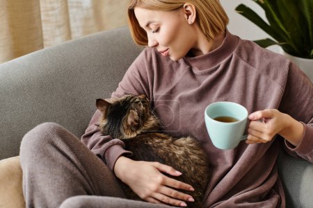 Una mujer elegante con el pelo corto se relaja en un sofá, saboreando café y abrazando a su gato.