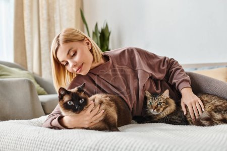 Une femme aux cheveux courts se relaxant sur un lit, accompagnée de deux chats affectueux.
