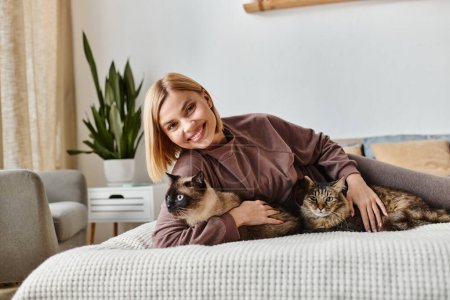 A woman with short hair relaxing on a bed, cuddling with two cats at home in a peaceful moment.